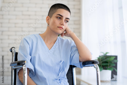 Sad caucasian patient with sitting in wheelchair in hospital room, sick adult woman in medical gown looking away, healthcare for mobility impairment, unhappy female with depression and mental stress.