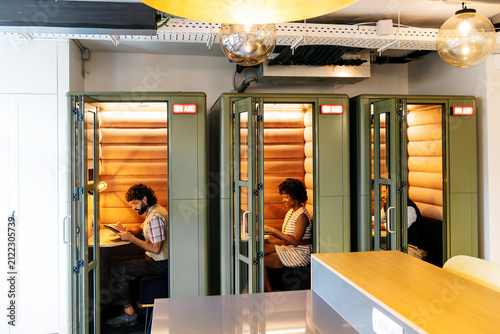 Diverse business professionals using acoustic booths for focused work, productivity, and privacy in a shared coworking space