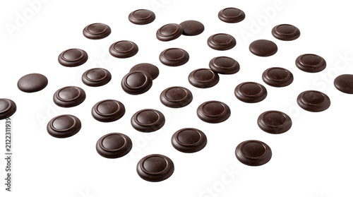 Numerous small dark chocolate callets scattered on a clean white surface.
