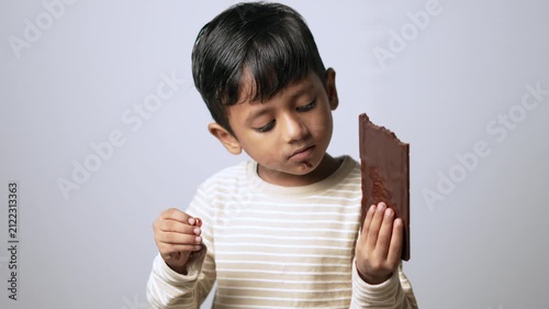 Indian boy eating chocolate bar. Happy child enjoying sweet snack at home.