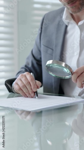 Mature man in suit carefully examining business document with a magnifying glass, analyzing contract details and terms for legal compliance or financial scrutiny
