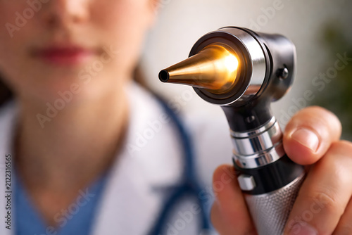 Doctor examining ear with otoscope during medical consultation in clinic close up