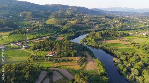 Lima River Meandering Through Lush Forested Valley And Verdant Agricultural Vineyards Of Ponte de Lima, Portugal. aerial arc shot