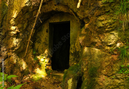 Foto Rectangular entrance to a dark tunnel carved into a mossy stone cliff face near Divje Jezero and Idrijca dam in Slovenia