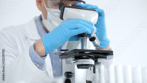 Принти на полотні Scientist in a lab coat and protective gear precisely adjusting a microscope, co