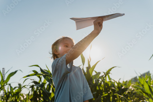 Canvastavla A curious young boy prepares to throw a white paper airplane while surrounded by a lush green cornfield