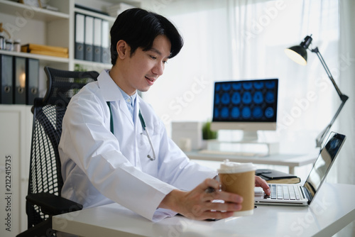 Doctor reviewing patient information on a laptop while completing medical paperwork in a modern clinic