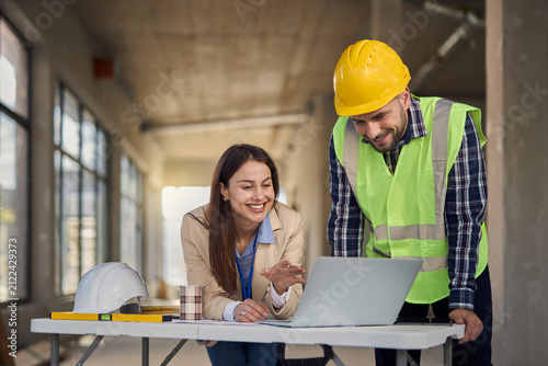 Female architect and building contractor using laptop at construction site