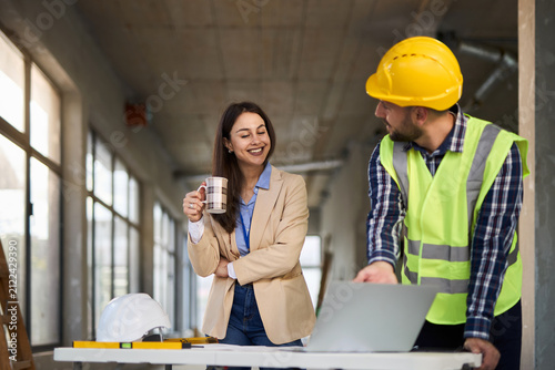 Female architect and building contractor using laptop at construction site