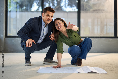 Young happy couple talking while analyzing housing plans at construction site.