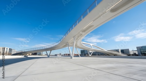 Modern pedestrian bridge with unique architectural design spanning over an empty concrete plaza under a bright blue sky