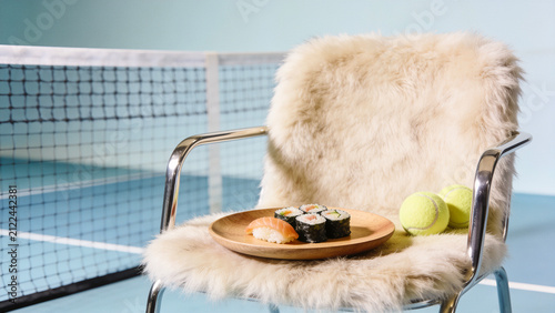 Sushi on a wooden plate on a furry chair on light pastel background. Lunch brake on tennis court. Retro style, minimalist, creative furniture. Salmon sashimi nigiri and maki rolls. Space for design