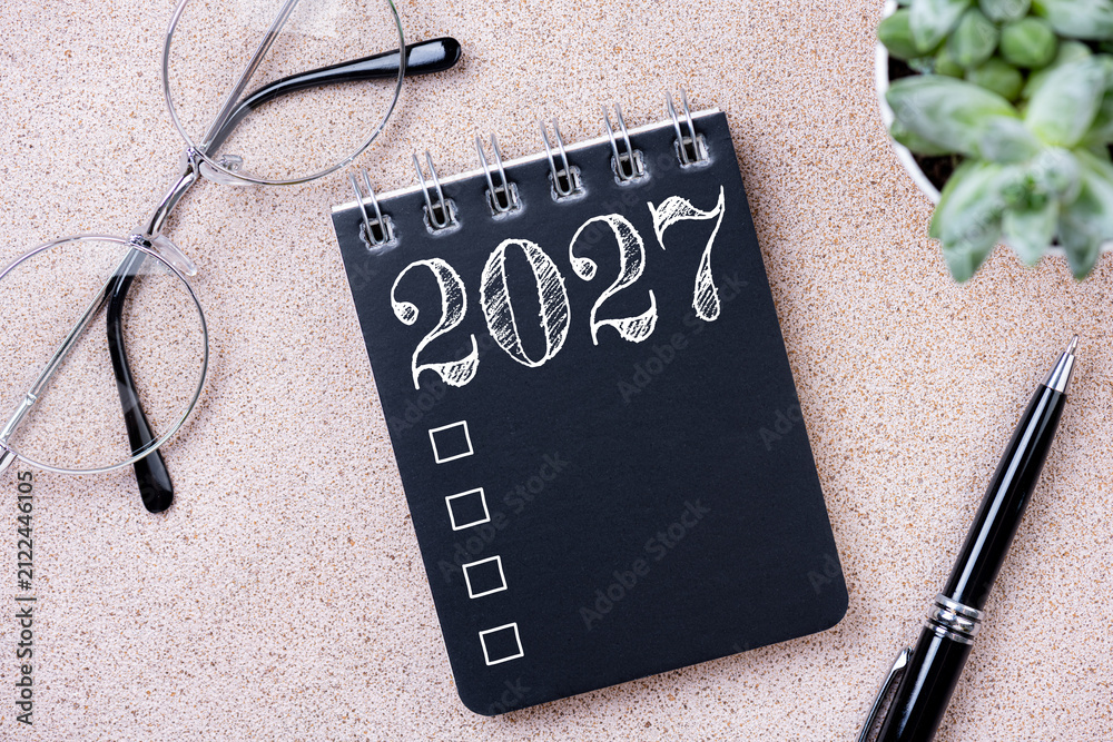 Fototapeta premium New year goals 2027. 2027 resolutions list with notebook, coffee cup, plant on table. Resolutions, plan, goals, action, checklist, idea concept. New Year 2027 resolutions, copy space