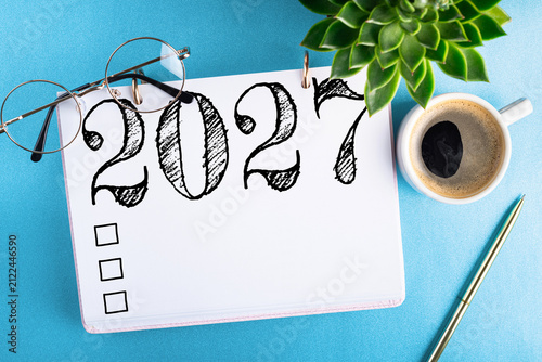 New year resolutions 2027 on desk. 2027 goals list with notebook, coffee cup, plant on blue table. Resolutions, plan, goals, action, checklist, idea concept. New Year 2027 resolutions. Copy space