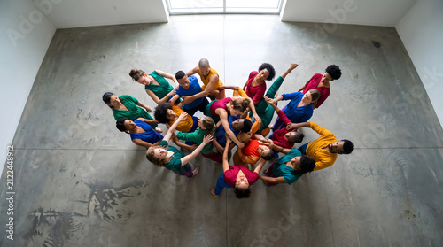 Group of people in colorful outfits forming a circle from overhead view performing dance poses