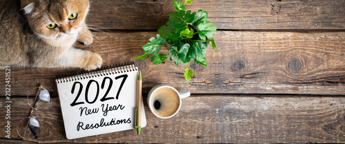 New year resolutions 2027 on desk. 2027 resolutions list with notebook, coffee cup, cute cat on table. Goals, resolutions, plan, cozy, hygge concept. New Year 2027 background