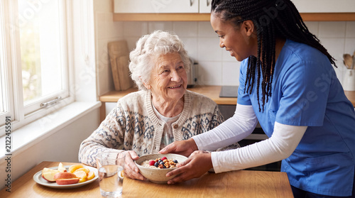 Caregiver serving a nutritious breakfast bowl to a happy senior woman in her home, promoting health and independent living