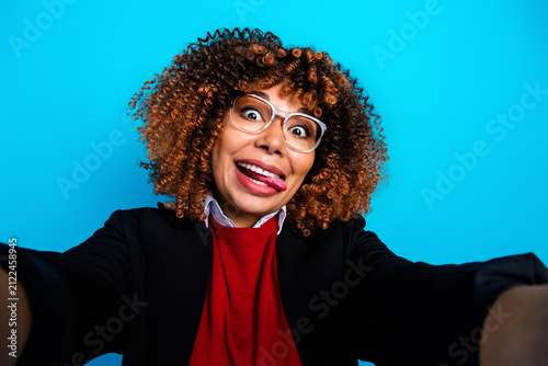 Fotografie Playful young woman making a funny face selfie with curly hair and glasses again