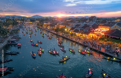 Hoi An Ancient Town at sunset, aerial view of traditional colorful lantern boats on the Thu Bon River with illuminated historic architecture, Vietnam.