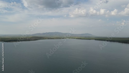 Panoramic view of a vast calm lake with distant hills under overcast sky.