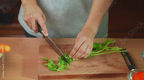 Woman hands were chopping fresh cilantro on a wooden cutting board.