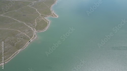 Aerial view of a grassy shoreline meeting calm greenish sea water.