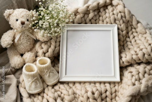 Baby announcement mockup with white picture frame, teddy bear, booties, and baby's breath on chunky knit blanket