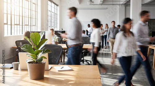 A beautifully detailed photorealistic stock photograph capturing a bustling open-plan office floor with a dynamic motion blur effect on walking employees in the background.