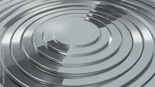 Abstract silver metallic concentric rings form a polished circular geometric background with layered grooves, reflective surfaces, and a futuristic industrial design pattern
