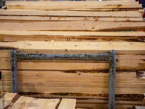 Obraz na płótnie Rough cut unfinished wooden boards with natural bark edges are stacked horizontally behind a grey metal rack inside a industrial sawmill facility