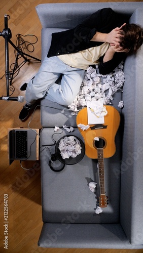 Quadro su tela Frustrated musician covering face with hands, lying on a sofa surrounded by crum