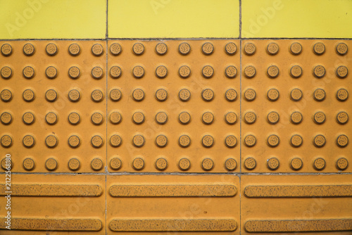 Konstfotografi Close-up of tactile paving with raised circular bumps and ridged lines on a yellow tiled surface for visually impaired navigation, urban accessibility design, public transport safety feature