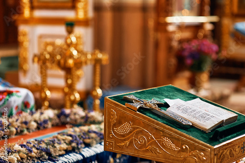 Obraz na płótnie Ornate gold crucifix and open gospel book rest on green velvet altar lectern inside  Orthodox church, surrounded by floral decorations and warm lit sanctuary details conveying reverence and tradition