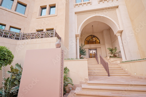 Photography Elegant entrance of a luxury hotel with Arabic architectural design, featuring arched doorways, intricate patterns, and lush greenery
