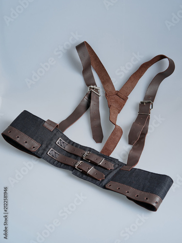 Black textile harness belt with brown leather straps and twin buckle closures displayed flat on a neutral background, showing functional fastening construction.