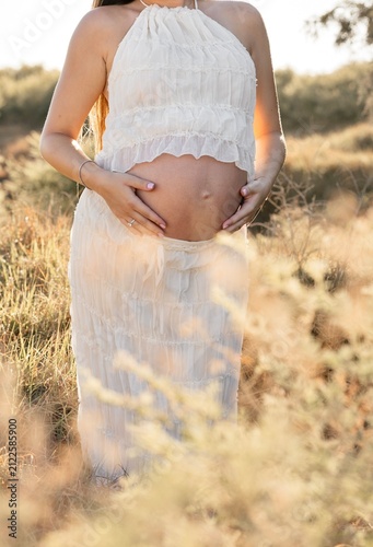 Woman hiking her pregnant belly in the meadow field 