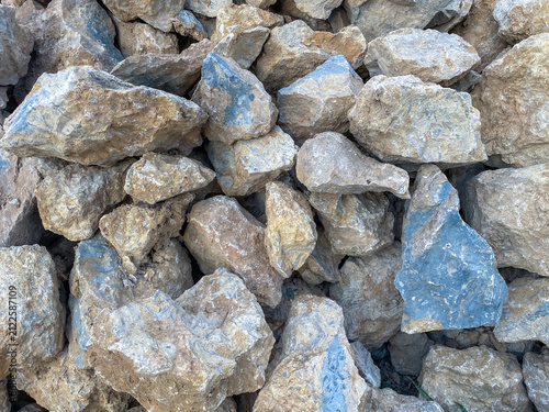Foto Pile of rough limestone rocks and construction stones with natural texture, brown and blue gray color