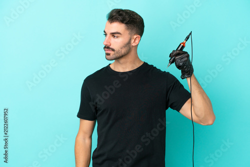 Fotografía Young tattoo artist man isolated on blue background looking to the side