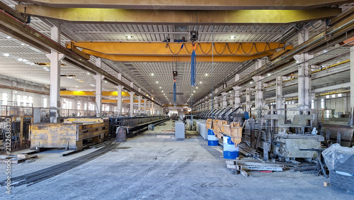 Industrial factory workshop interior with yellow overhead bridge crane and heavy manufacturing equipment.
