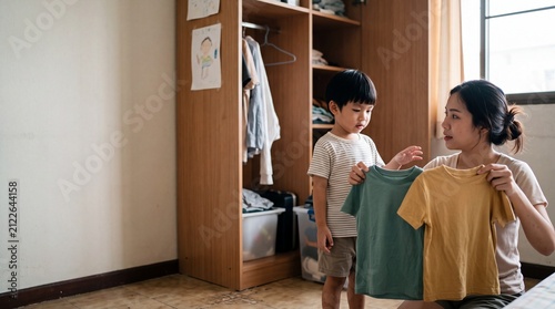 A mother helps her young child choose a t-shirt from a wooden wardrobe, showcasing a tender moment of everyday life and domesticity.