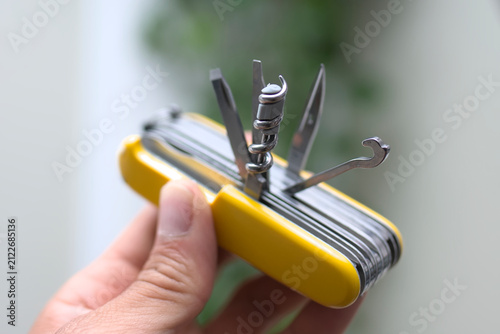 Person holding multipurpose swiss style army knife with yellow handle and open tools with copyspace for text