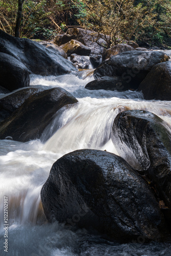 Cuadro en lienzo Close-up vertical shot of white water cascading through large dark river rocks
