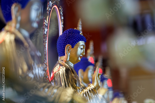 Vietnam Quoc Tu Pagoda. A row of Buddhas in golden robes with midnight-blue ushnishas. The teaching gesture multiplies infinitely in the dim light of the sanctuary. Ho Chi Minh City, Vietnam.