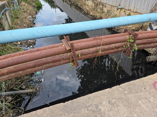 фотографія Rusty and Blue Industrial Pipes Crossing Over a Drainage Canal