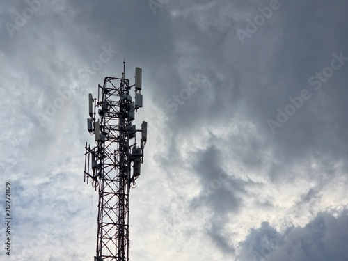 A telecommunications cell tower equipped with various antennas against a dramatic, cloudy sky.