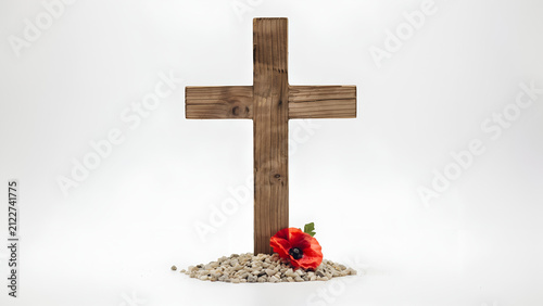 Wooden cross with a single poppy flower and small stones during remembrance day concept