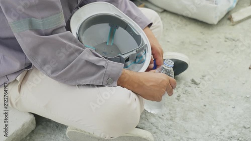 Person sitting home inspector helmet water bottle concrete site inspection calm break worker holding hard hat outdoor safety scene tired construction job site breaks