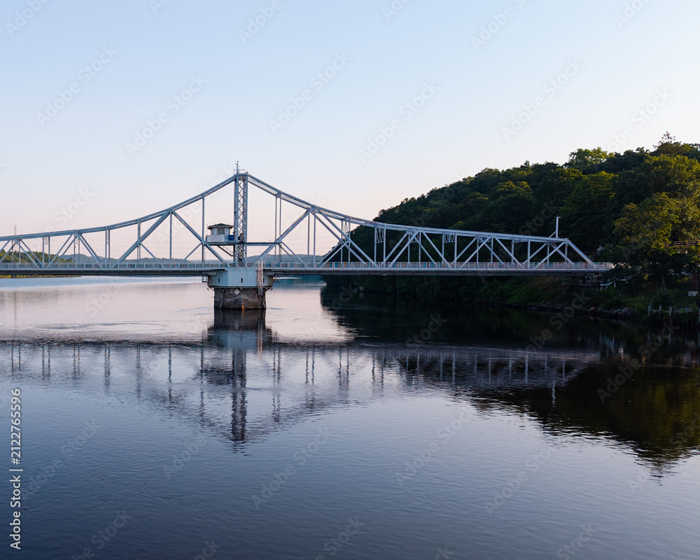 Fototapeta premium Summer aerial view featuring the East Haddam Swing Bridge along the Connecticut River in East Haddam, Connecticut just after sunrise