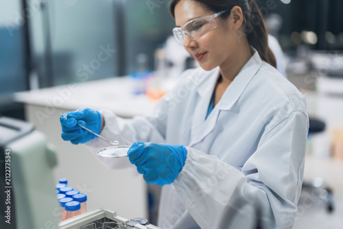 Professional female scientist examining chemical powder on a watch glass in sterile laboratory. Advanced pharmaceutical research and quality control testing for biotechnology industry.