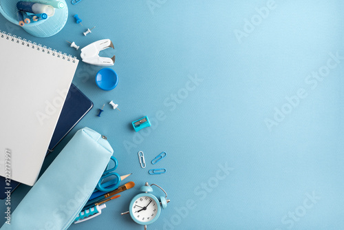 A flat lay of school and art supplies on a blue background with a notebook pencil case and alarm clock